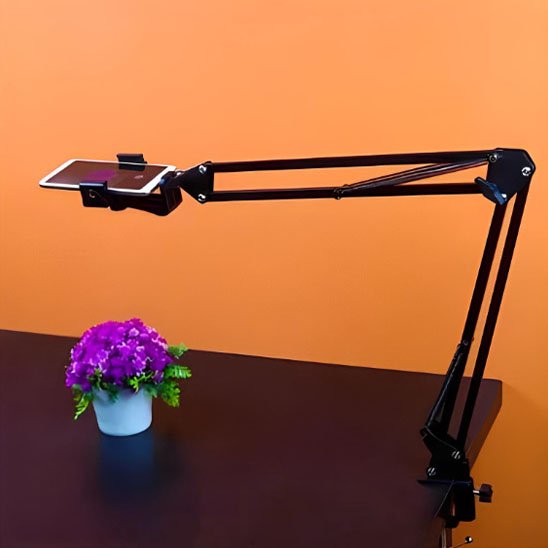 Support articulé pour téléphone fixé à un bureau, filmant une plante fleurie en pot sur fond orange pour une prise de vue produit