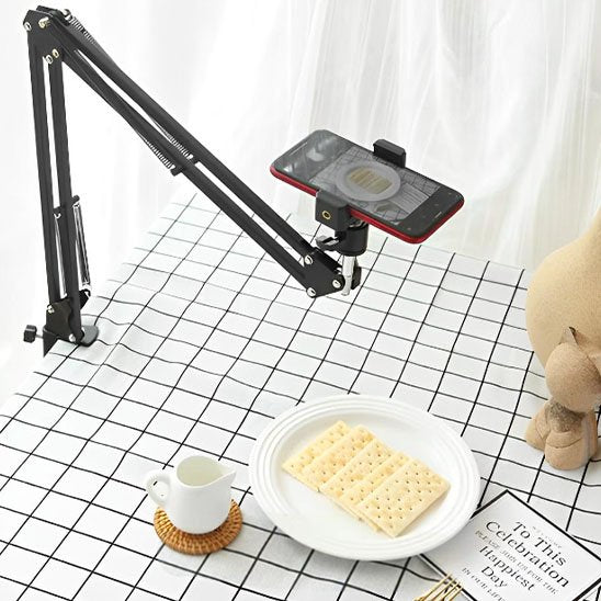 Support articulé pour téléphone fixé à une table, capturant une vue de dessus d’un plat avec biscuits, tasse de lait et peluche décorative